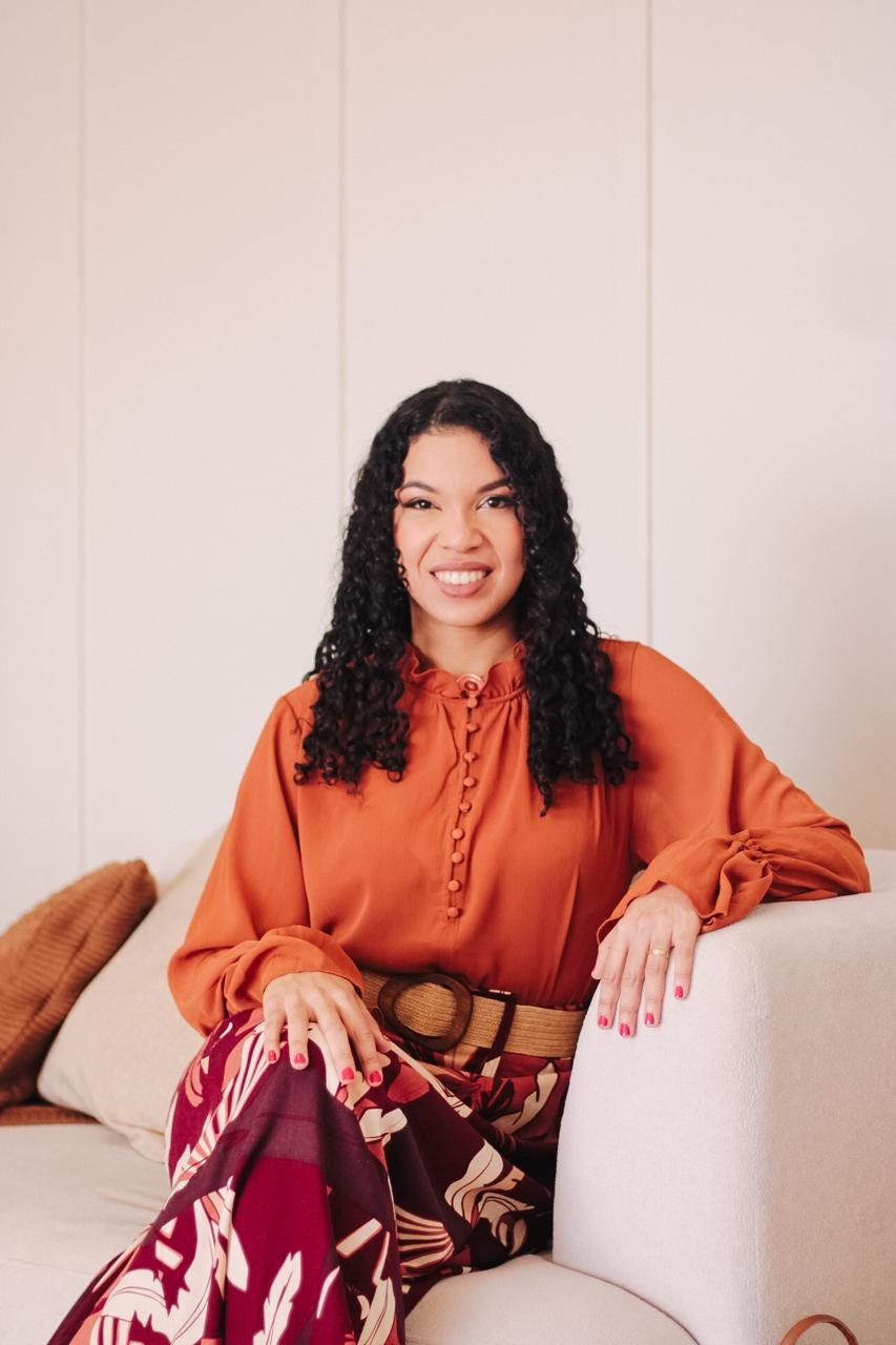 Retrato da Dra. Kárytta Ramos sorrindo, sentada em uma poltrona clara